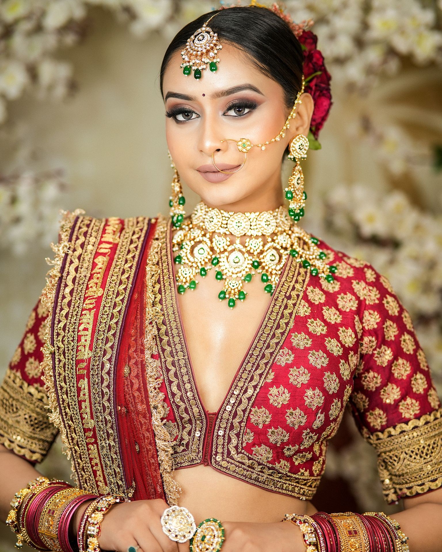 Woman in traditional ornate red bridal attire with gold embroidery and elaborate jewelry.